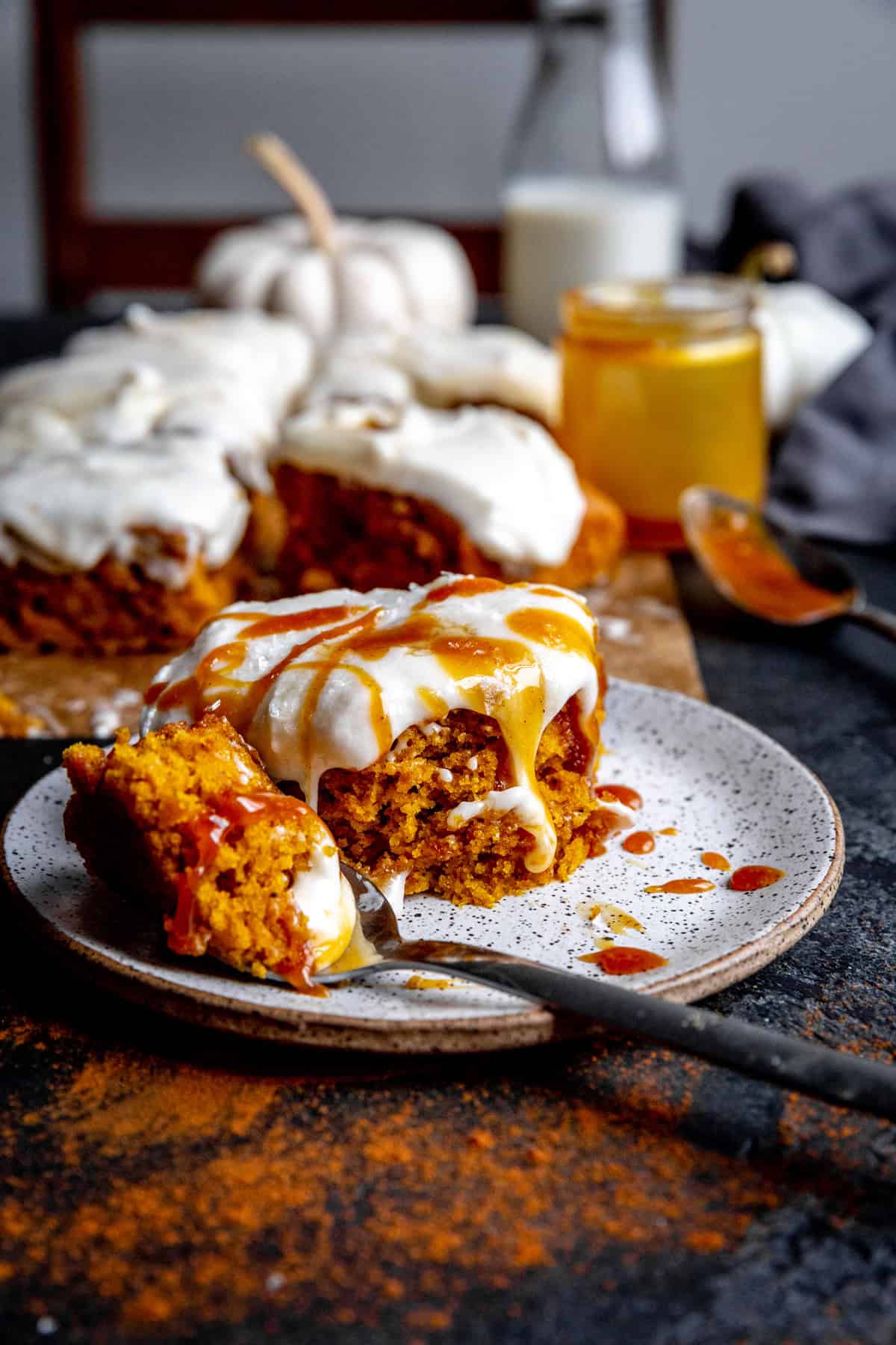 Slice of pumpkin cake drizzled with caramel on a white plate with a fork.