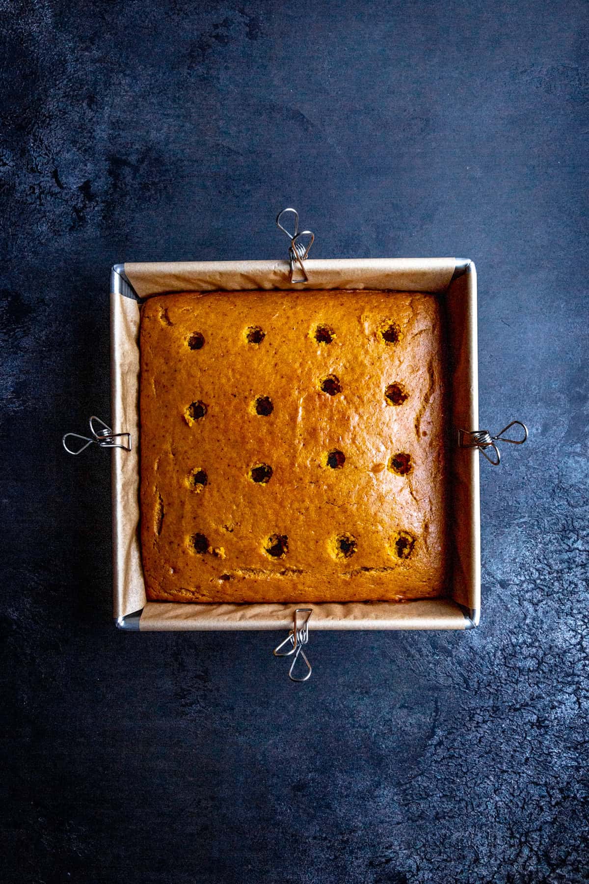 Pumpkin cake in a square pan with holes poked in it.