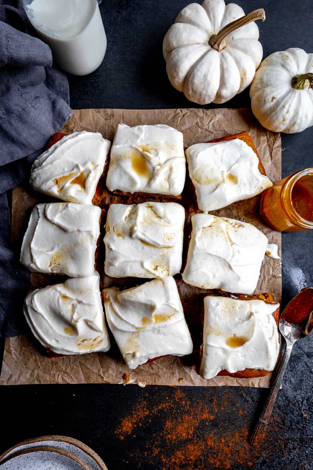 Frosted pumpkin cake squares, small white pumpkins and a glass of milk.