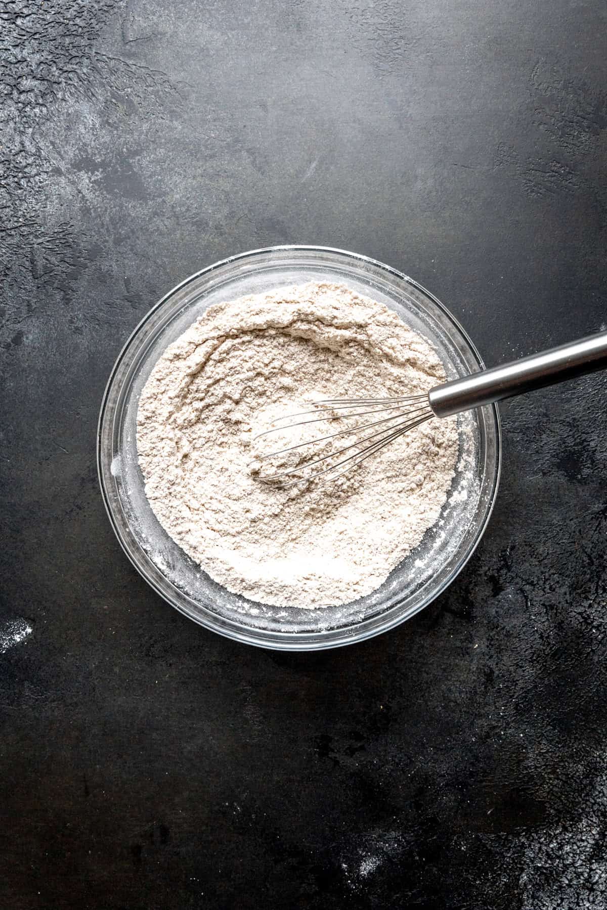 Glass bowl of flour and a wire whisk.