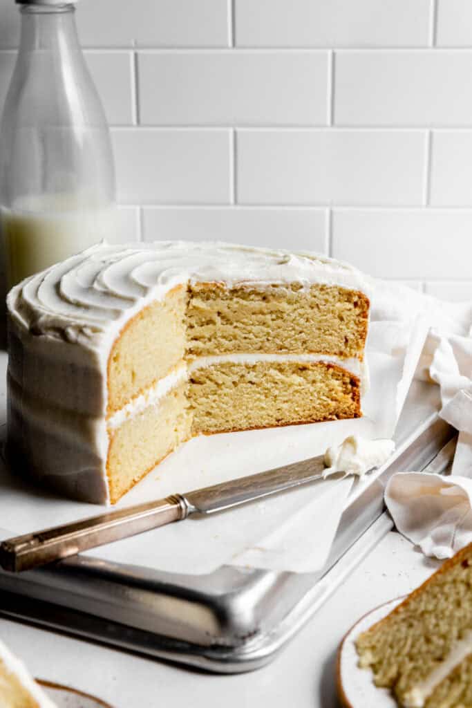 Vanilla cake on a baking sheet and a knife covered in frosting.