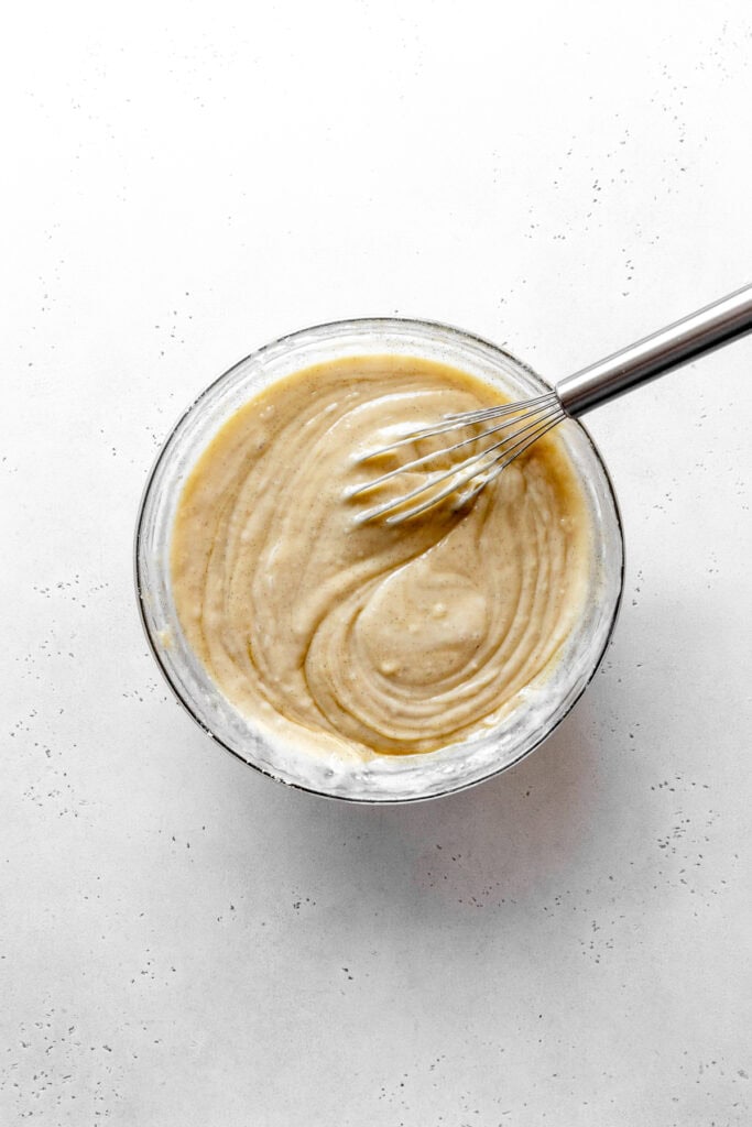Vanilla cake batter in a glass bowl with a wire whisk.