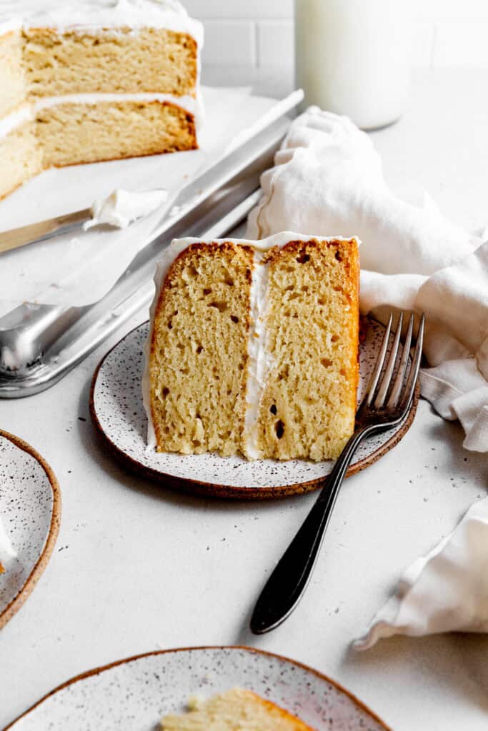 Slice of vanilla cake on a white plate with a fork.