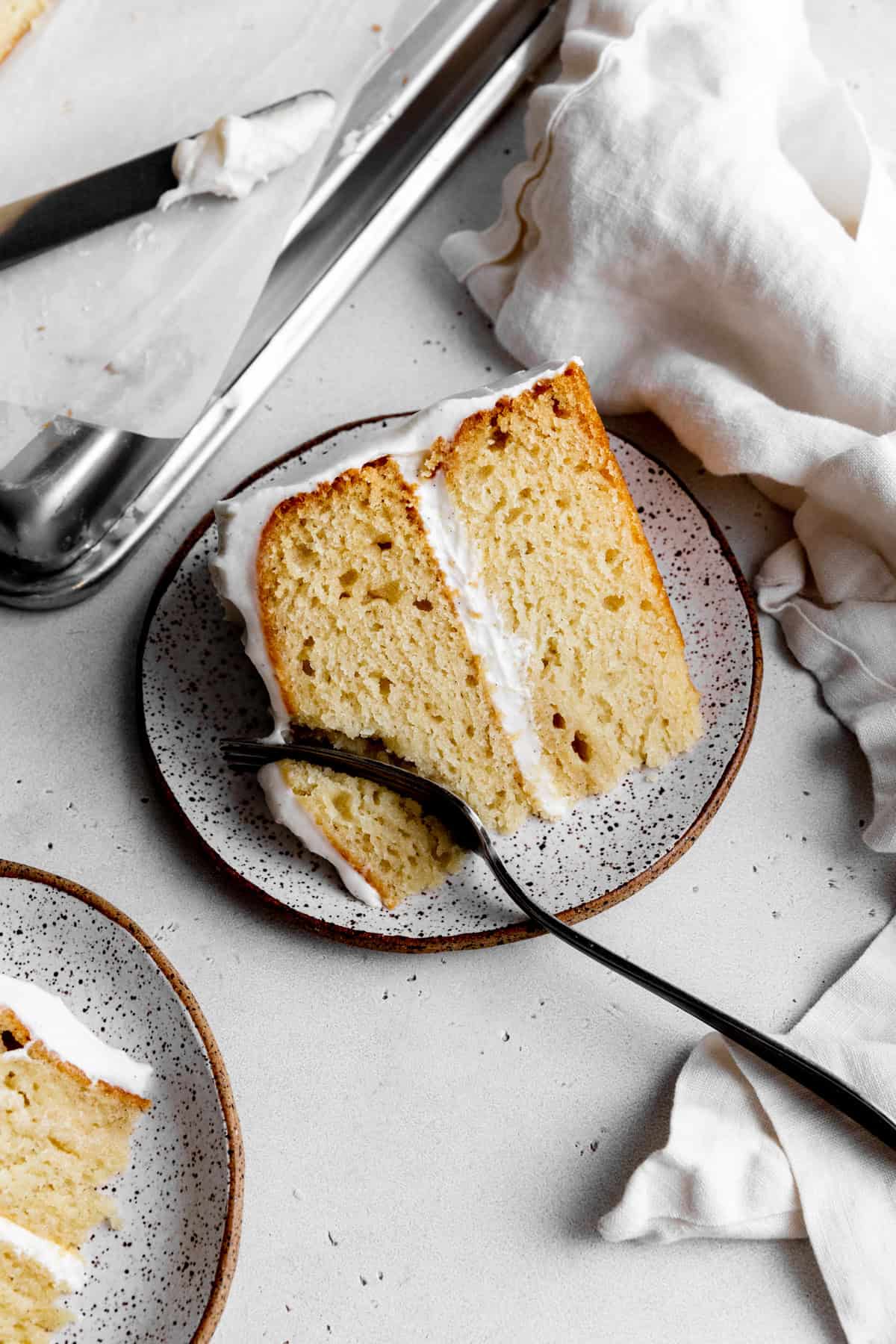 Fork cutting into a piece of vanilla layer cake.