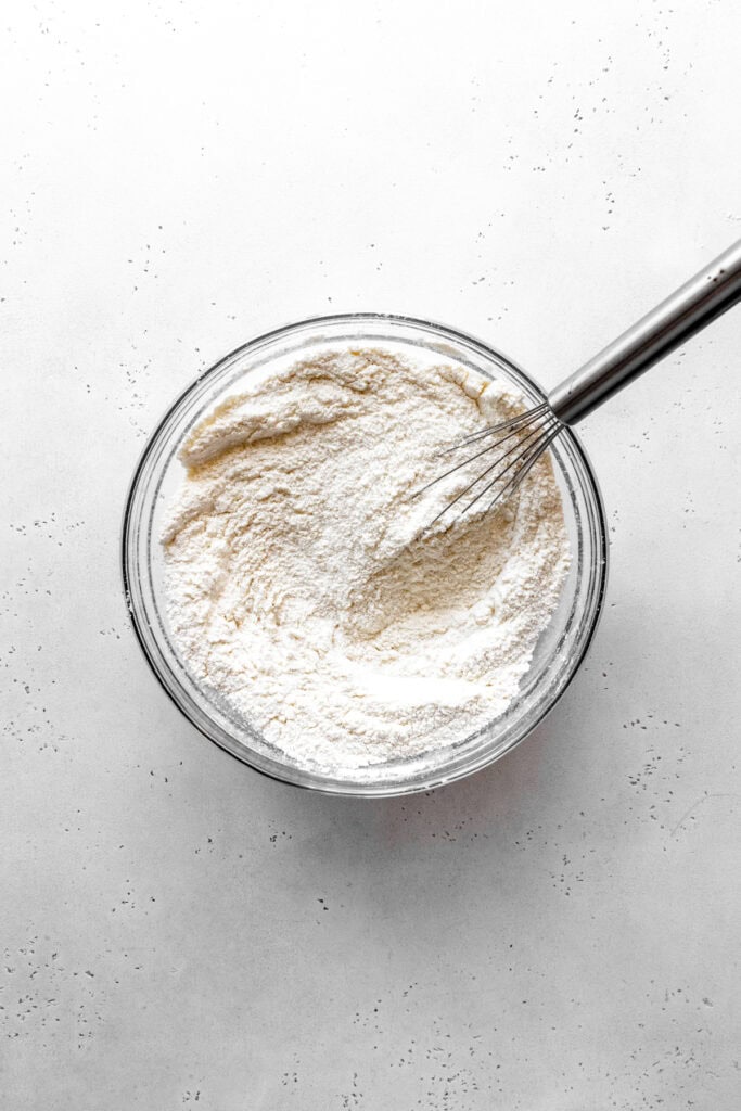 Flour in a glass bowl with a wire whisk.