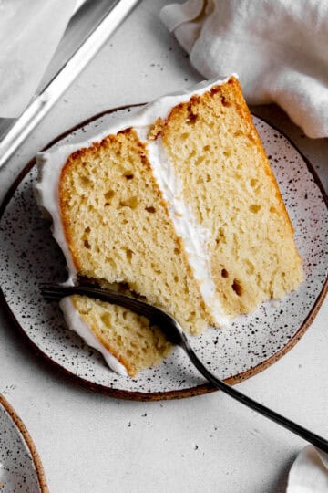 Fork cutting into a slice of vanilla layer cake on a plate.