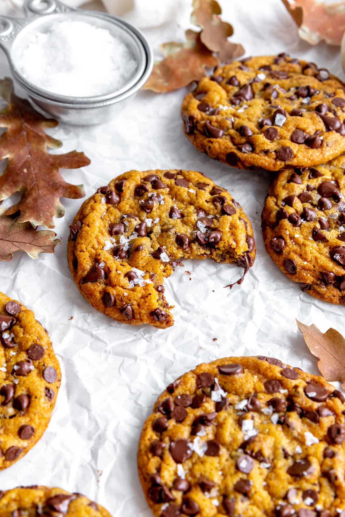 Pumpkin chocolate chip cookie with a bite taken out of it and a cup of salt.