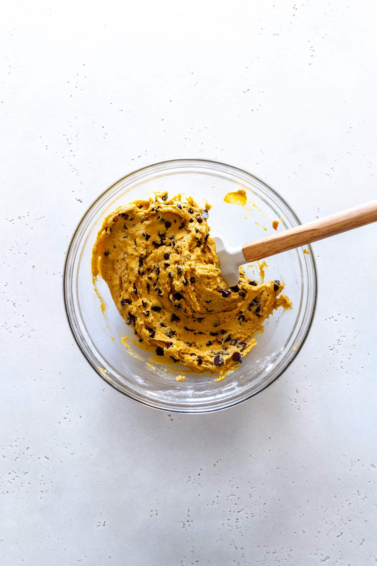 Rubber spatula in a glass bowl of pumpkin chocolate chip cookie dough.
