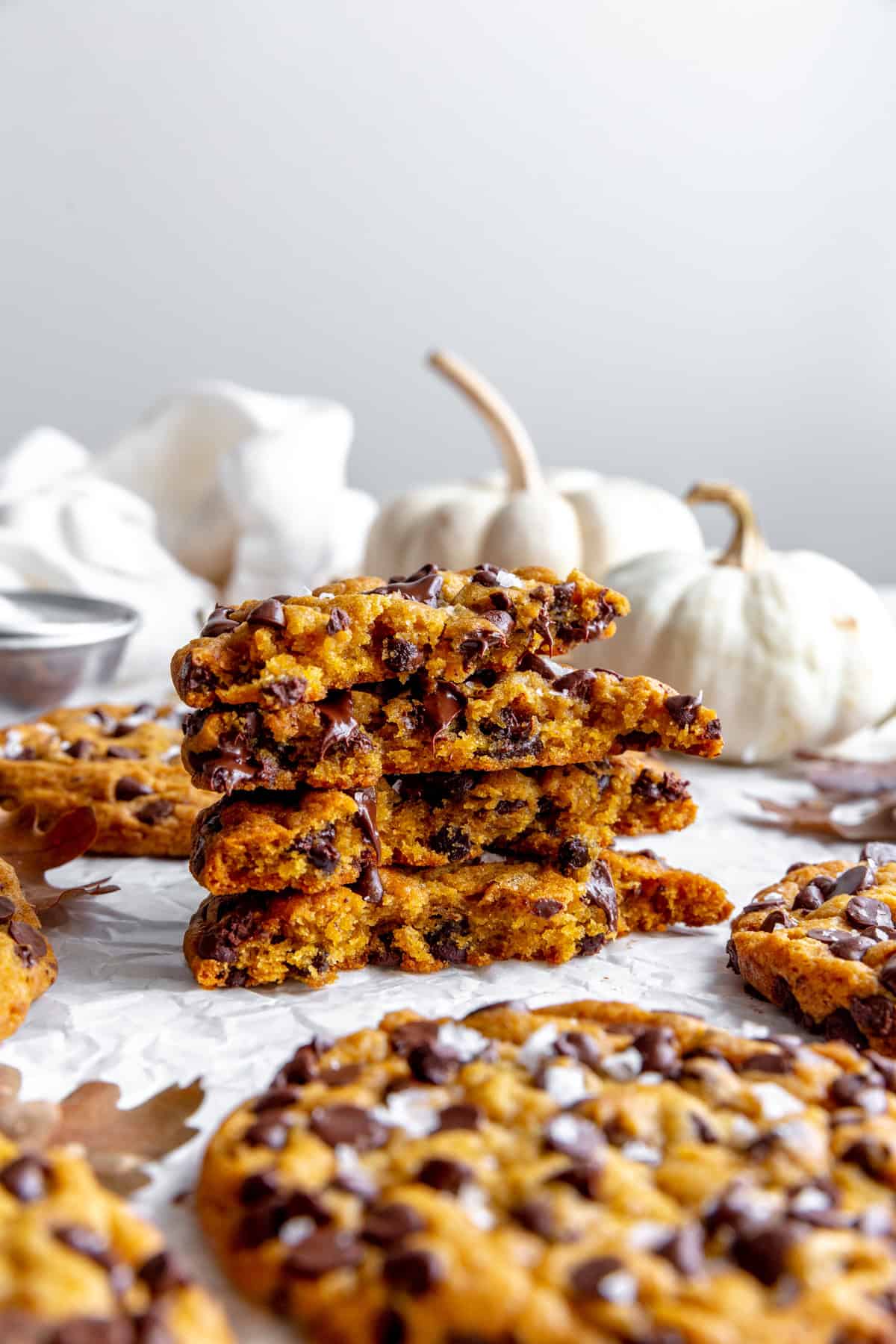 Stack of pumpkin chocolate chips cookies and two white pumpkins.