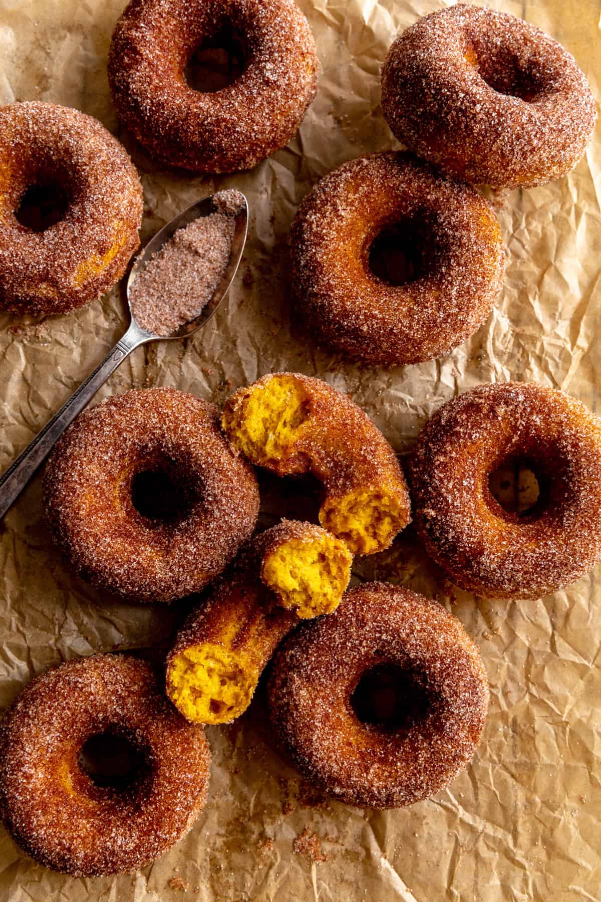 Pumpkin donuts on parchment paper and a spoon of cinnamon sugar.