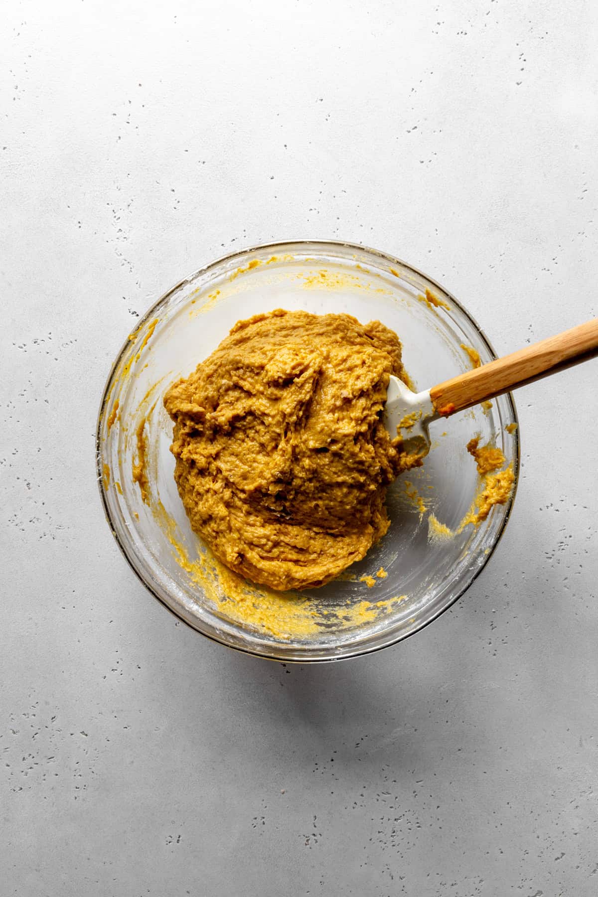Pumpkin donut batter in a glass bowl with a rubber spatula.