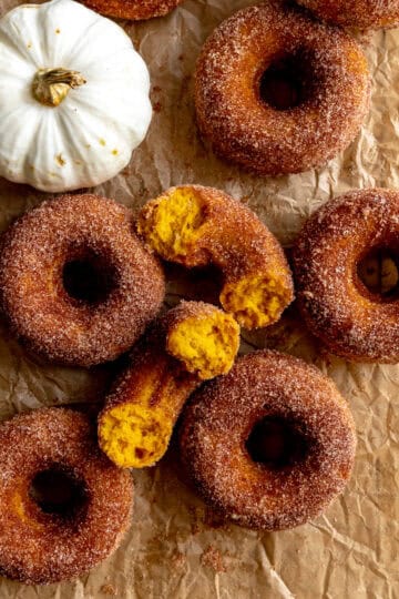 Pumpkin donuts on parchment paper and a white pumpkin.