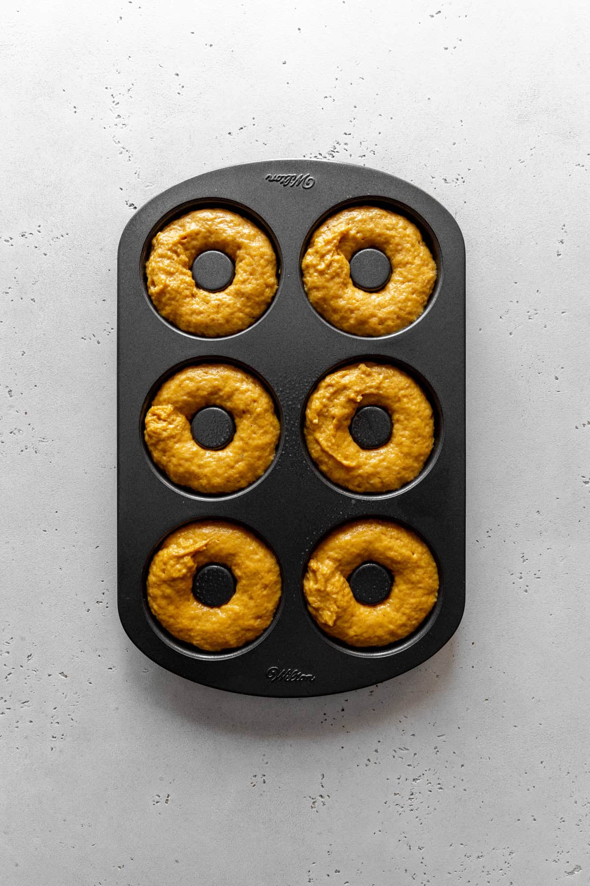 Unbaked pumpkin donuts in a donut pan.