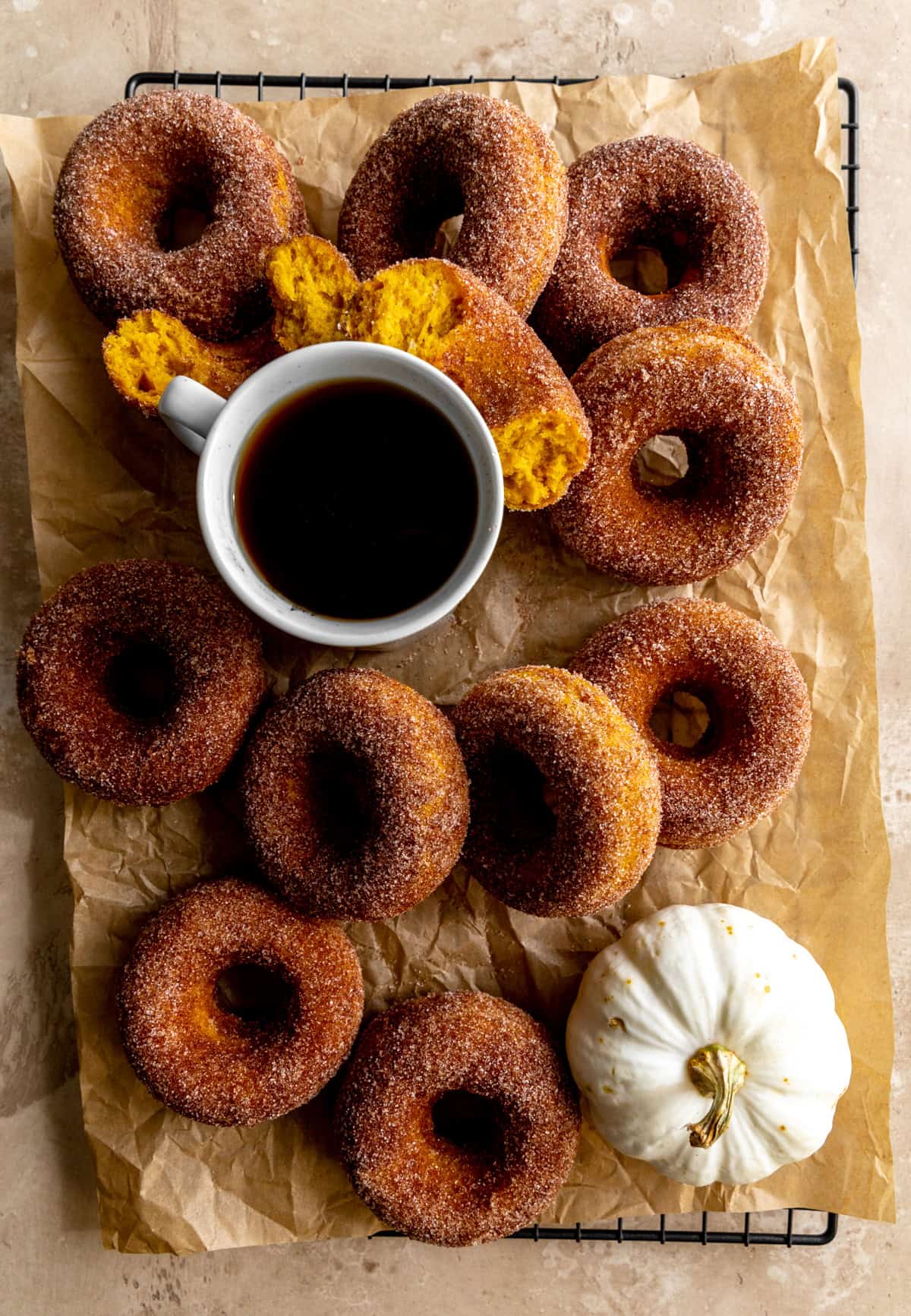 Pumpkin donuts on a cooling rack with a cup of coffee.