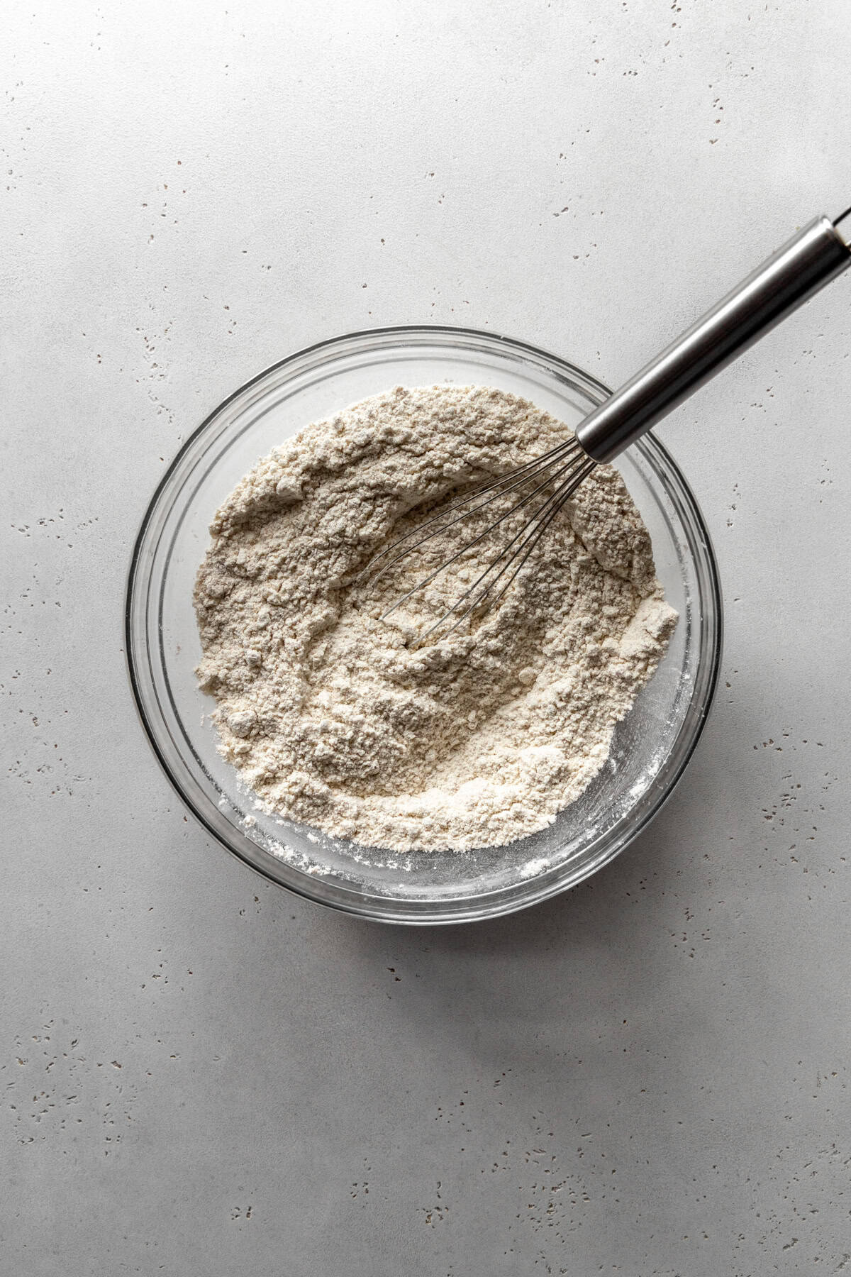 Glass bowl of flour with a wire whisk.