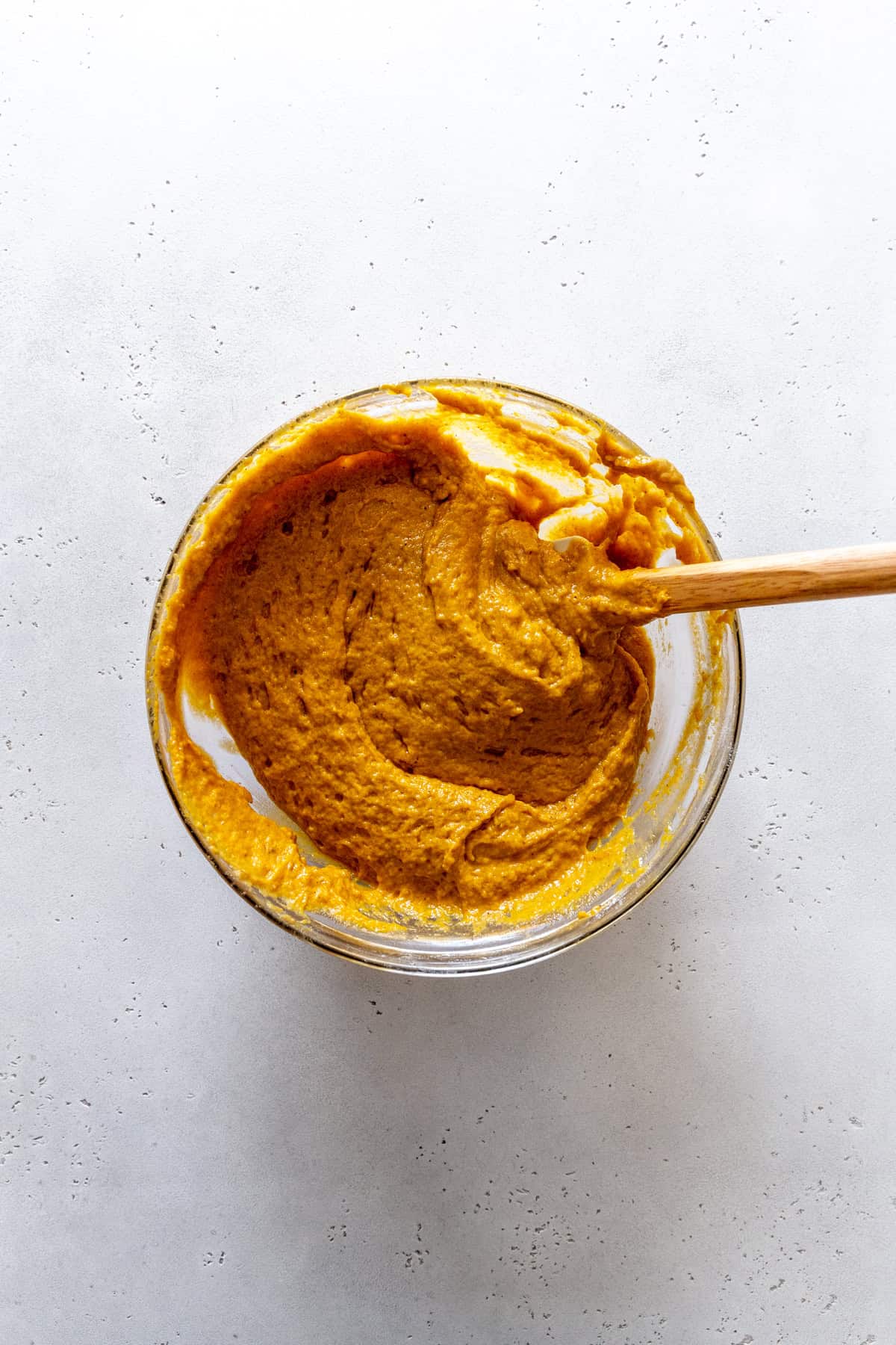 Rubber spatula in a glass bowl of pumpkin batter.