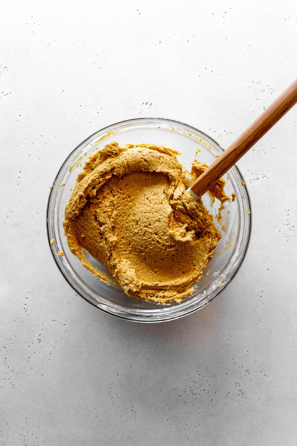 Pumpkin cookie dough in a glass bowl and a rubber spatula.