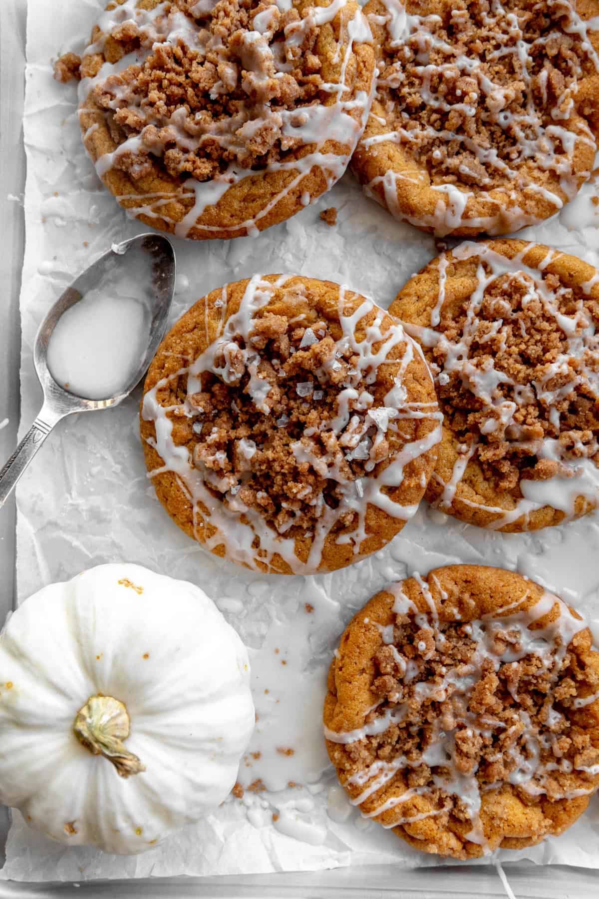 Pumpkin coffee cake cookies, a white pumpkin and a spoon full of glaze.