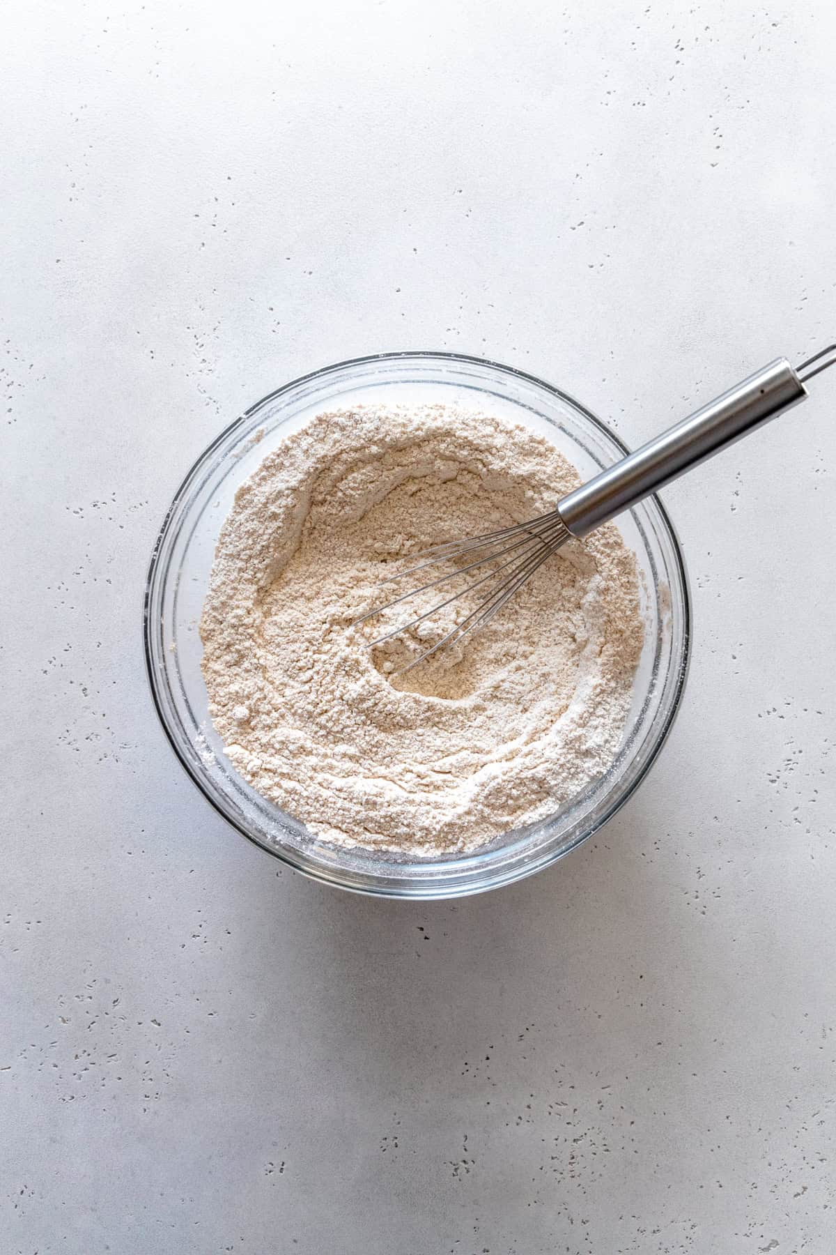 Wire whisk in a glass bowl of flour.