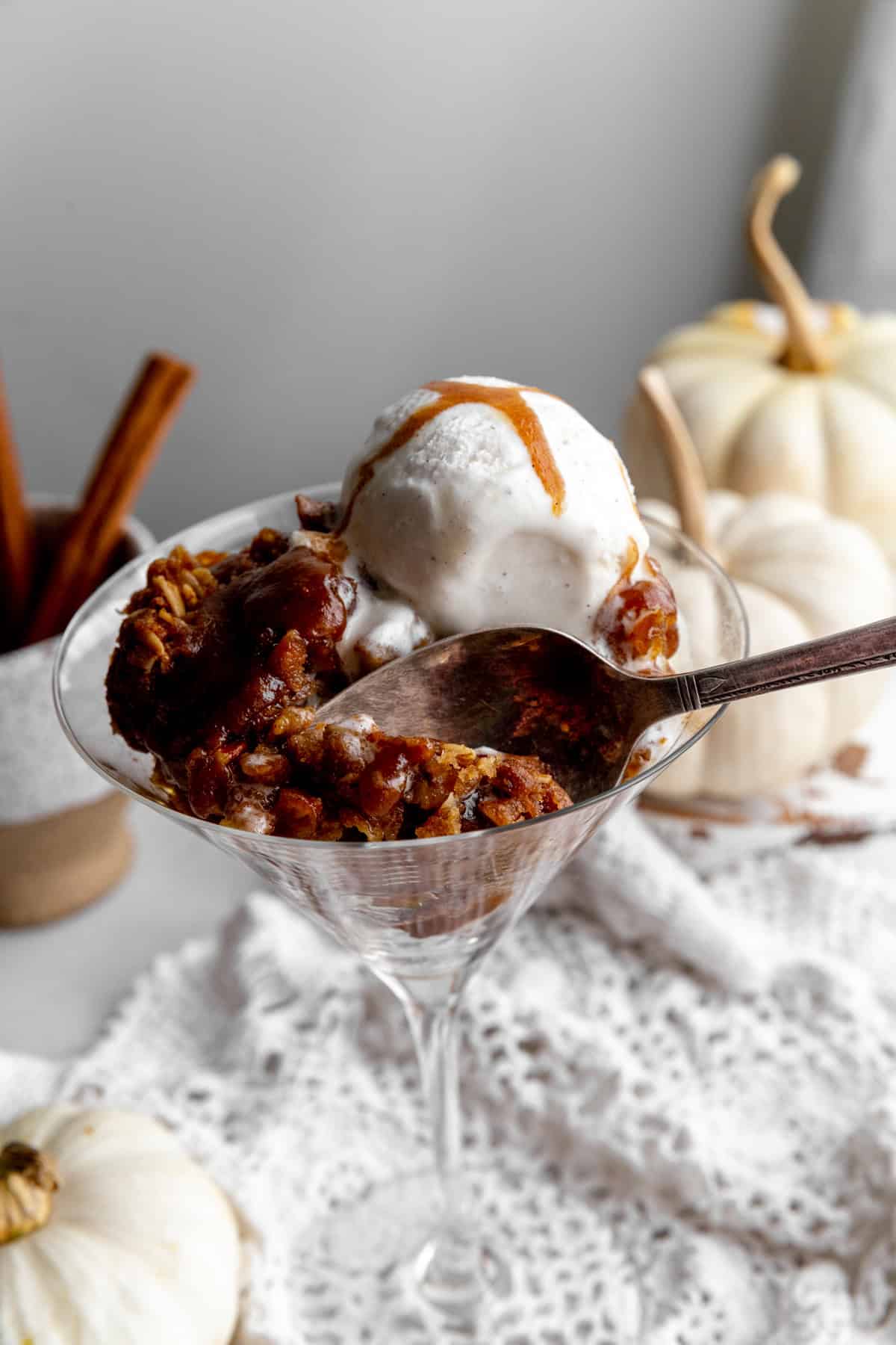 Spoon digging into pumpkin pecan crisp and two white pumpkins.