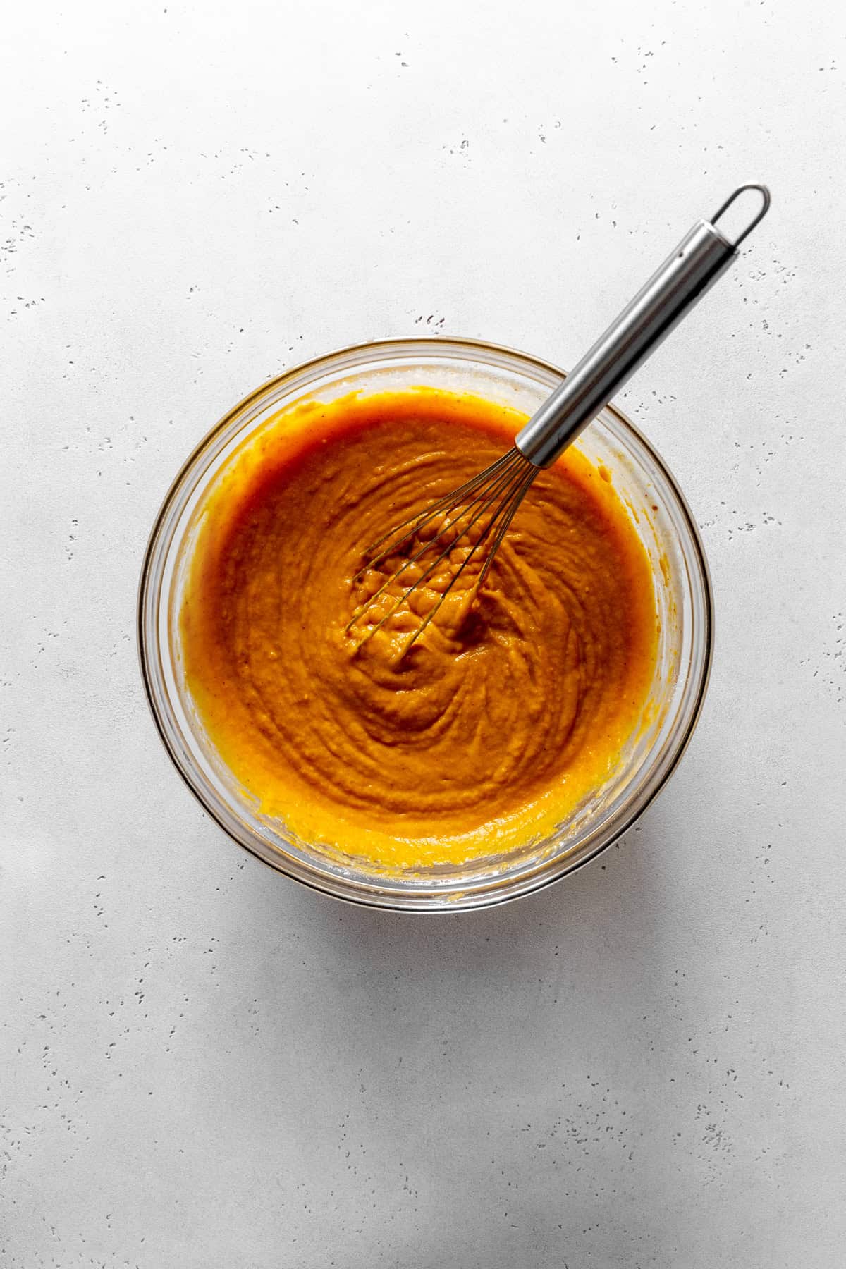Glass bowl of pumpkin puree in a glass bowl with a wire whisk.