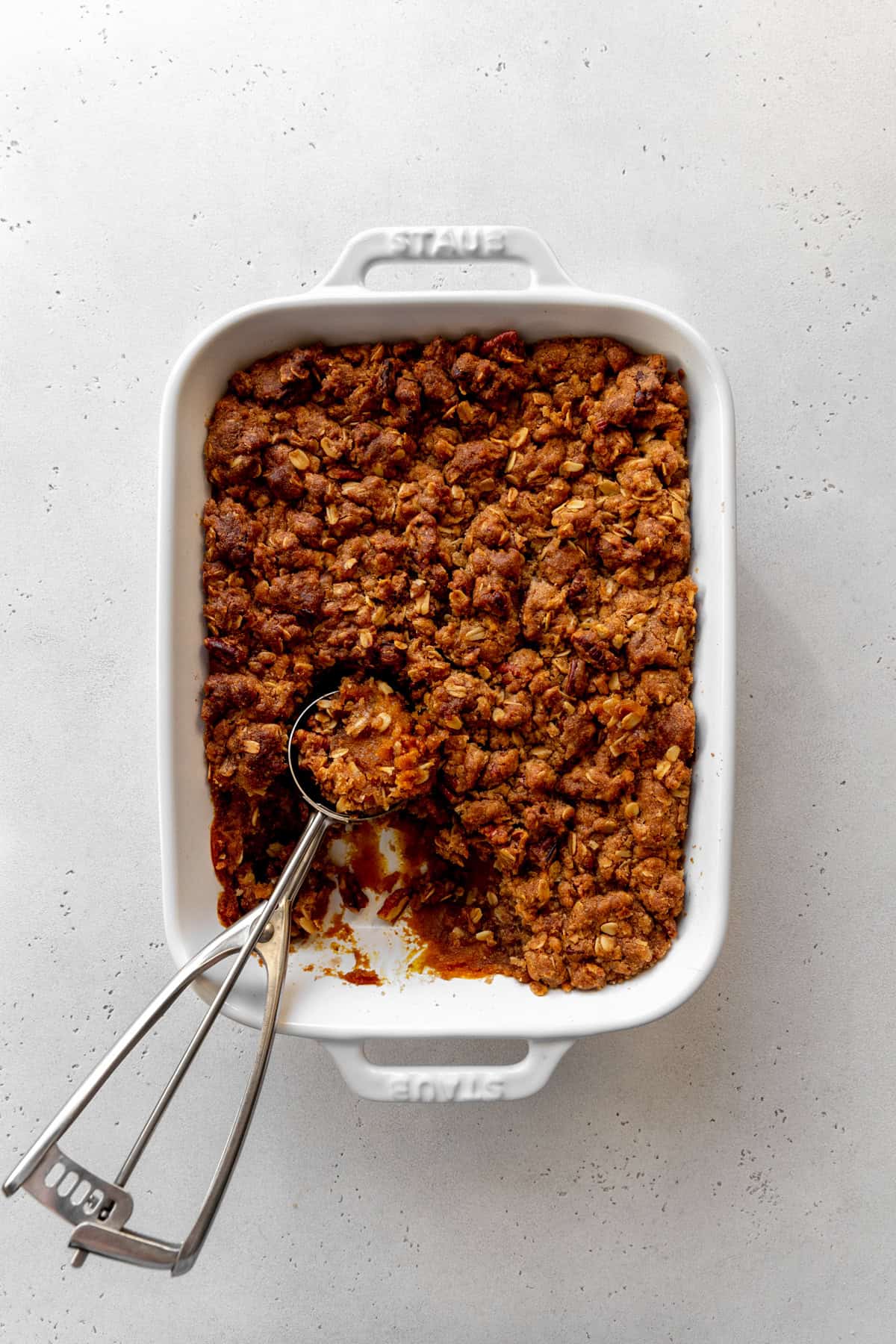 Baked pumpkin pecan crisp in a baking dish with a scoop.