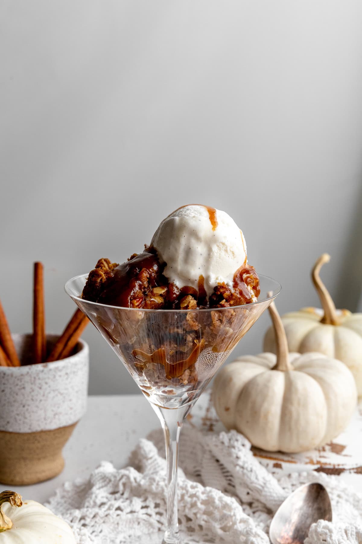 Pumpkin crisp topped with vanilla ice cream, two white pumpkins and cinnamon sticks.