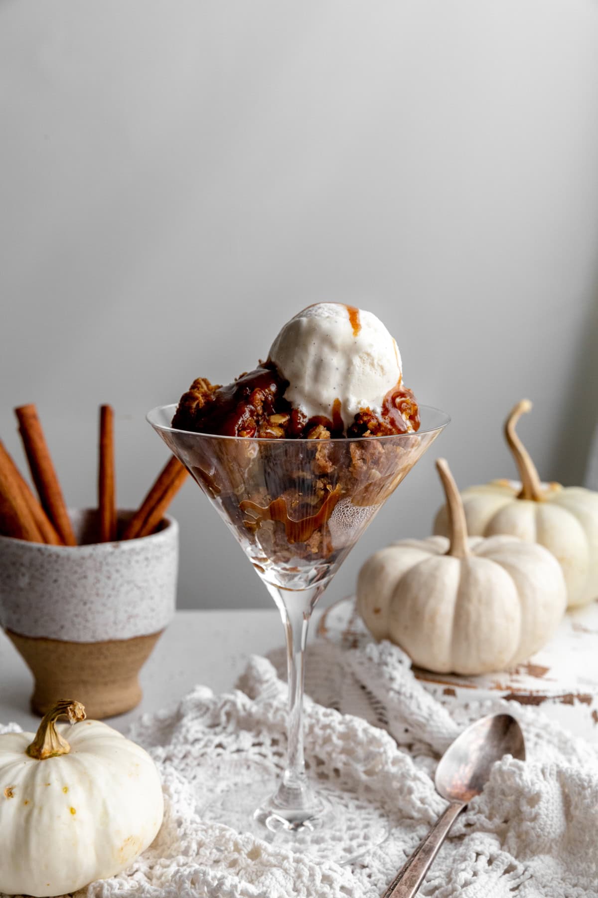 Pumpkin crisp in a martini glass, two white pumpkins and cinnamon sticks.