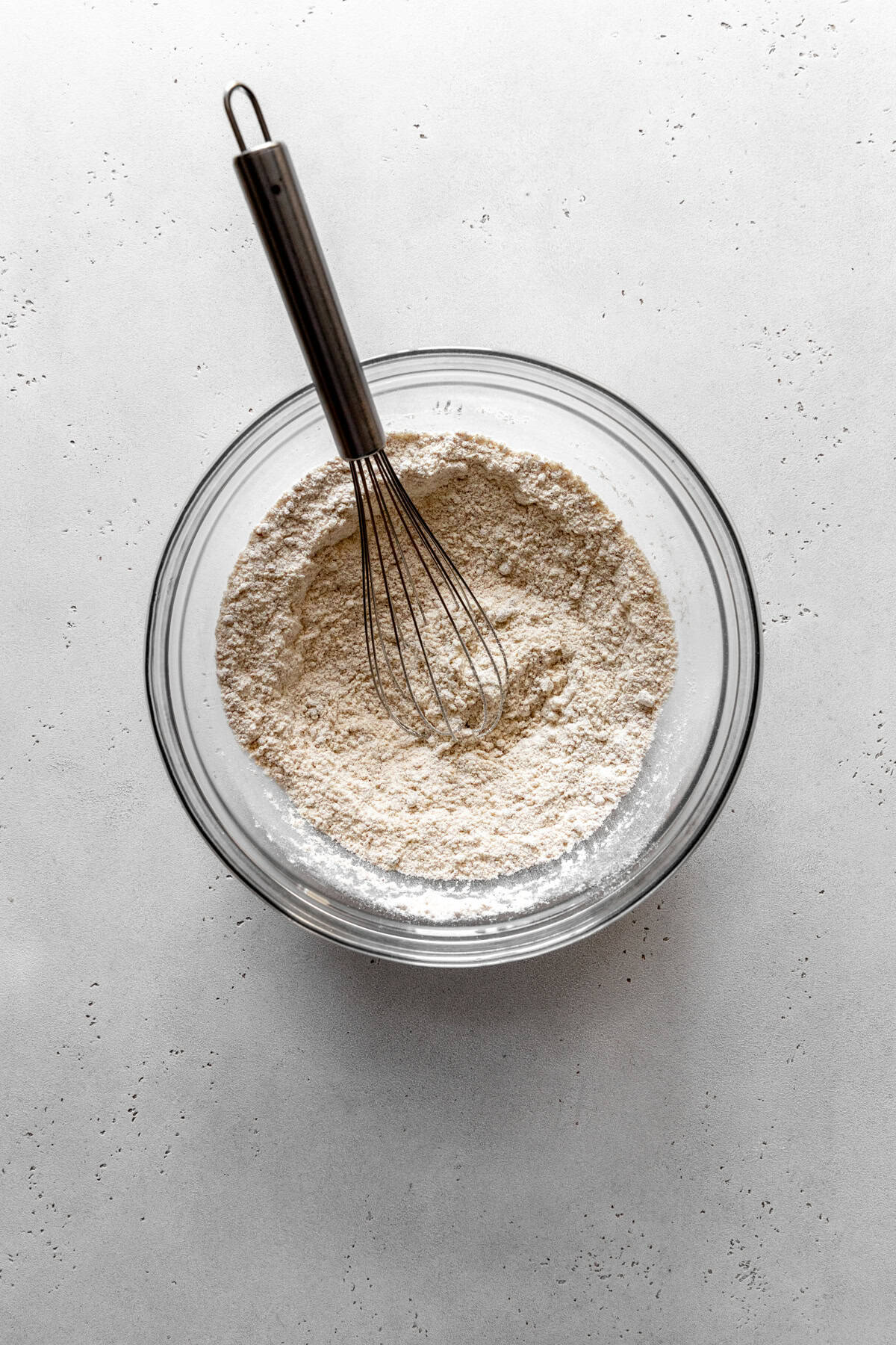Flour and sugar in a glass bowl with a wire whisk.